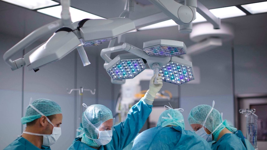 A group of surgeons stand around an operating table holding instruments