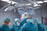 A group of surgeons stand around an operating table holding instruments