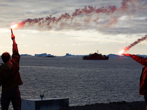 Two people wave flares in Antarctica as icebreaker vessel heads out to sea