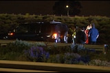 A dark coloured four wheel drive with its lights flashing as emergency service workers stand beside it