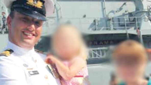 Gillett in uniform with his family (blurred) in front of the ship.
