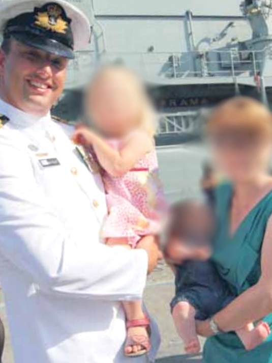 Gillett in uniform with his family (blurred) in front of the ship.