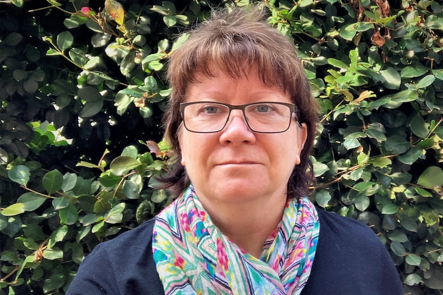 Headshot of woman against shrub backdrop.