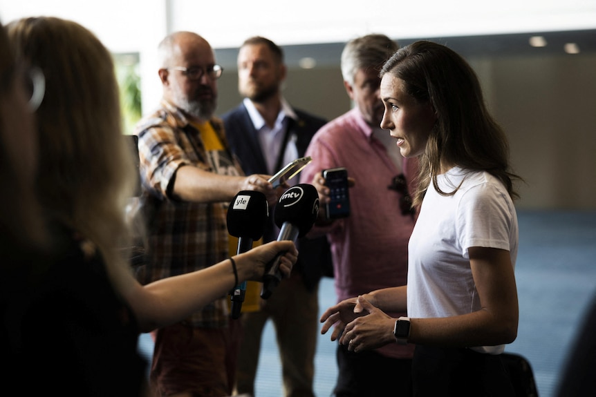 Sanna Marin talks to a pack of journalists holding microphones. 