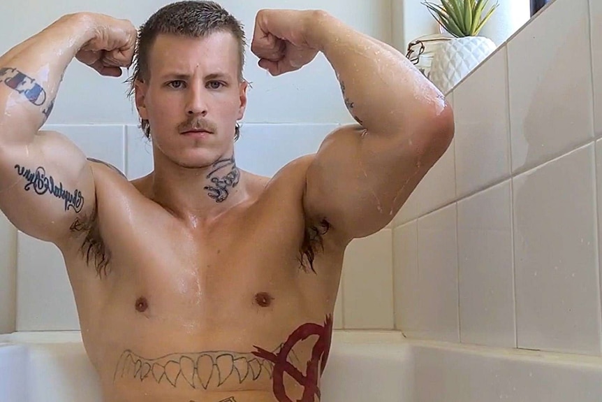 Alec Nysten poses in a bath topless, flexing his arms.