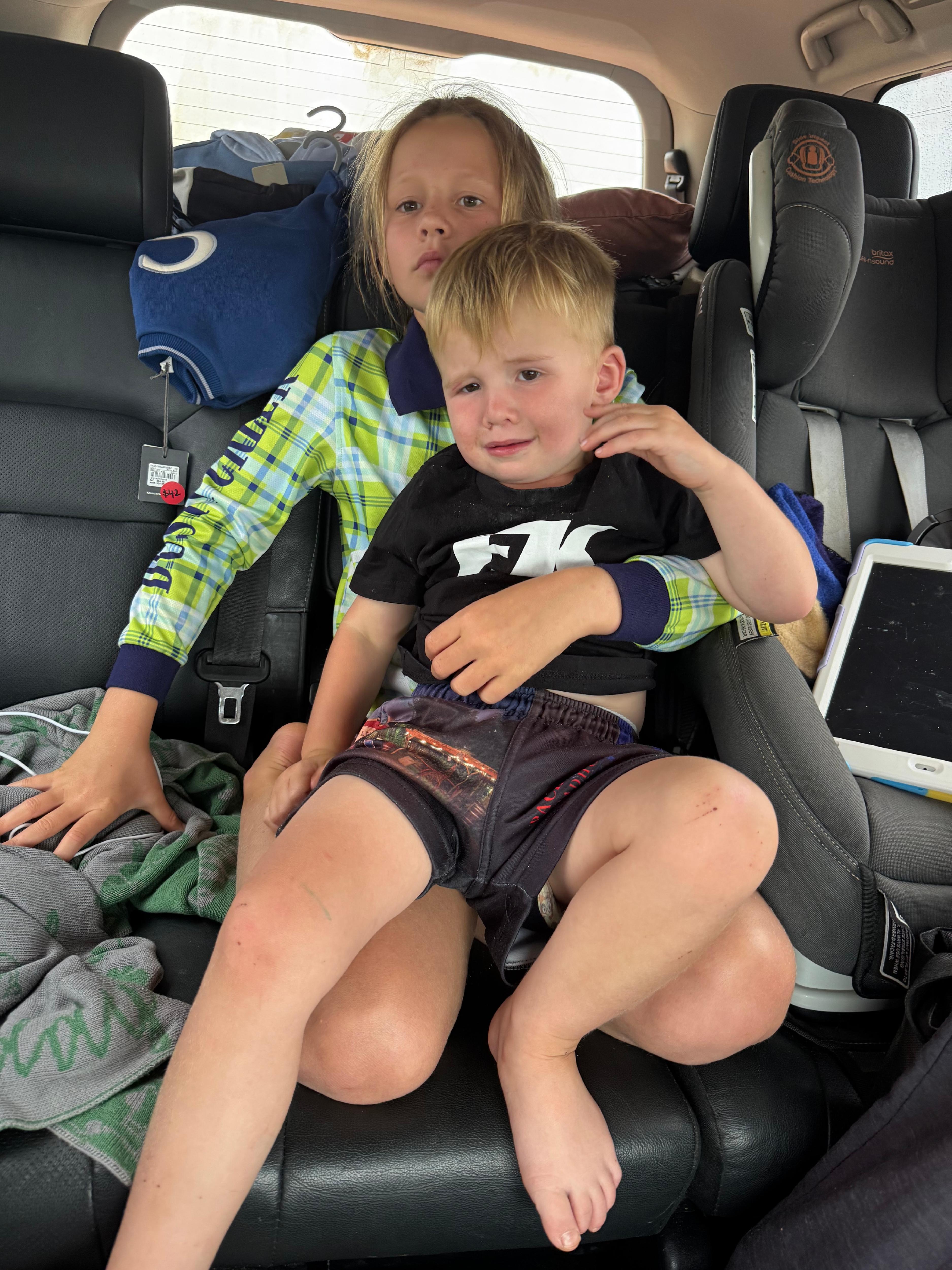 A young boy looks uncomfortable sitting in the lap of a young girl in the back of a car.