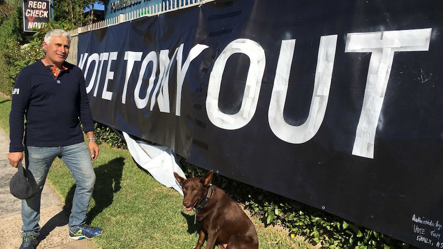 A man and his dog stand in front of a massive 'Vote Tony Out' poster