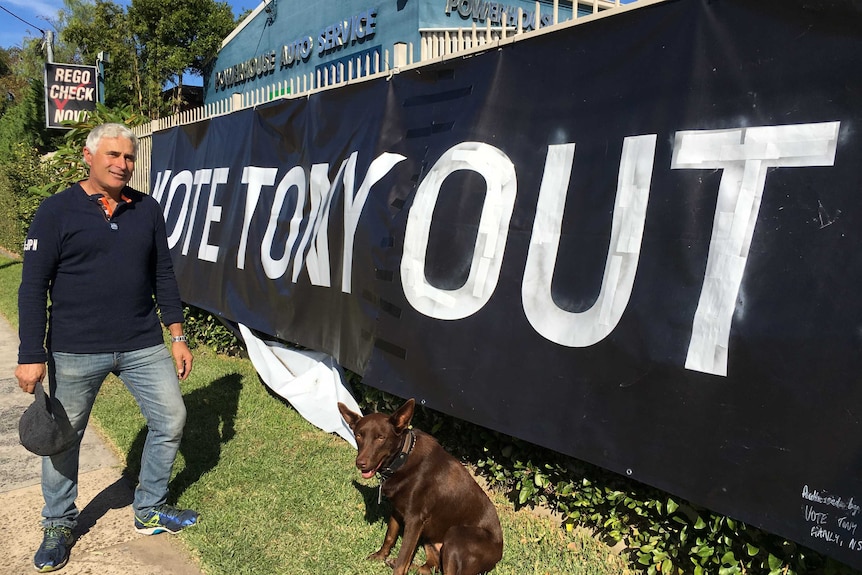 A man and his dog stand in front of a massive 'Vote Tony Out' poster