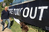 A man and his dog stand in front of a massive 'Vote Tony Out' poster