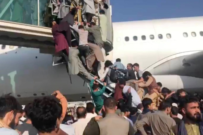 People cling to a plane staircase trying to board a departing flight from Kabul