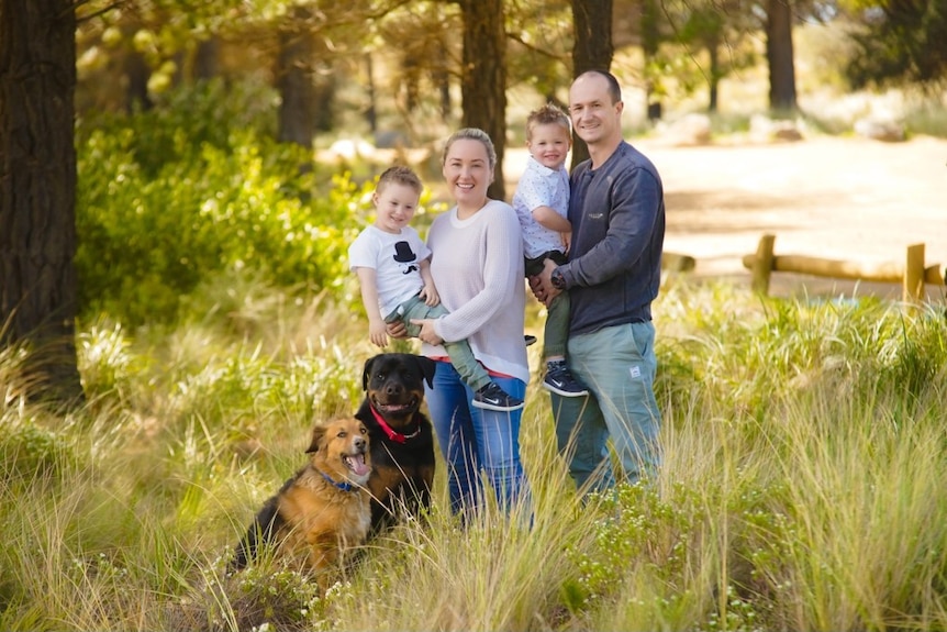 Family photo of husband and wife with two young children and two dogs standing in long grass