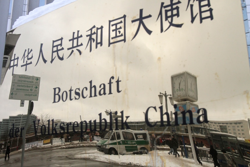 Un véhicule de police et des manifestants sont reflétés sur la plaque signalétique de l'ambassade de Chine en Allemagne.
