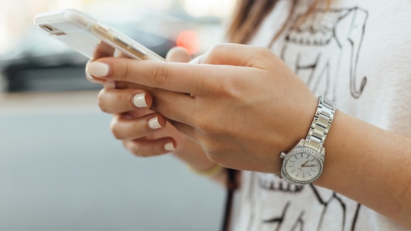 Close up of person holding phone in hands. Person wears a silver wrist-watch.