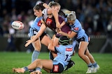 A maroons player is tackled by three blues players as she passes the ball