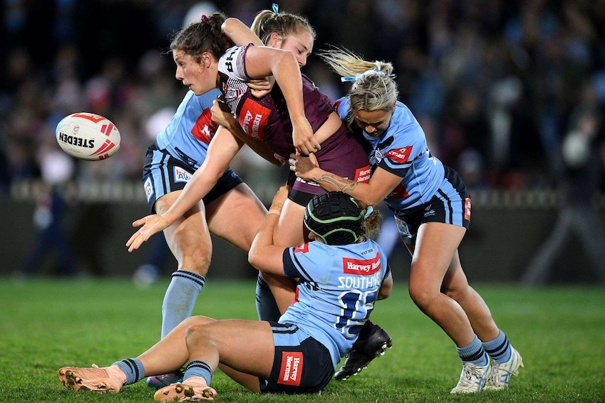 A maroons player is tackled by three blues players as she passes the ball