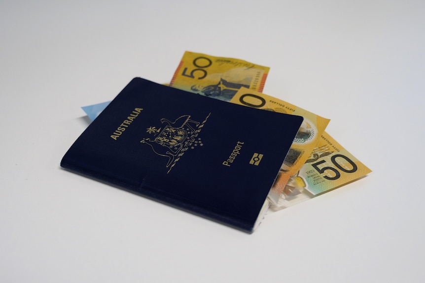 An Australian passport with money stuffed inside, on a white table.