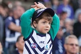 A young boy in a Fremantle guernsey holds his arms over his head amongst the crowd.