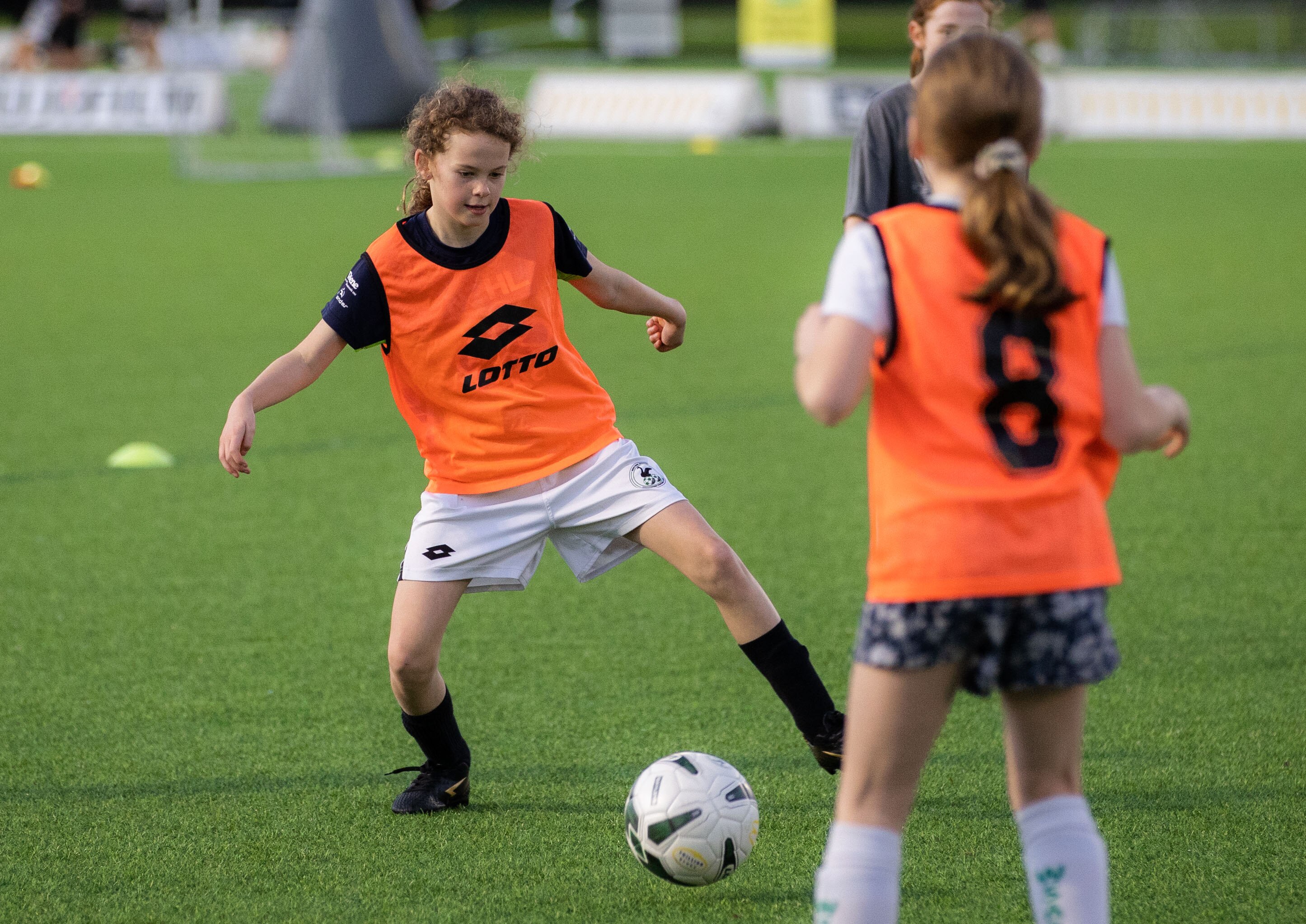A young female football player looks to kick a ball at the goals at a training session.