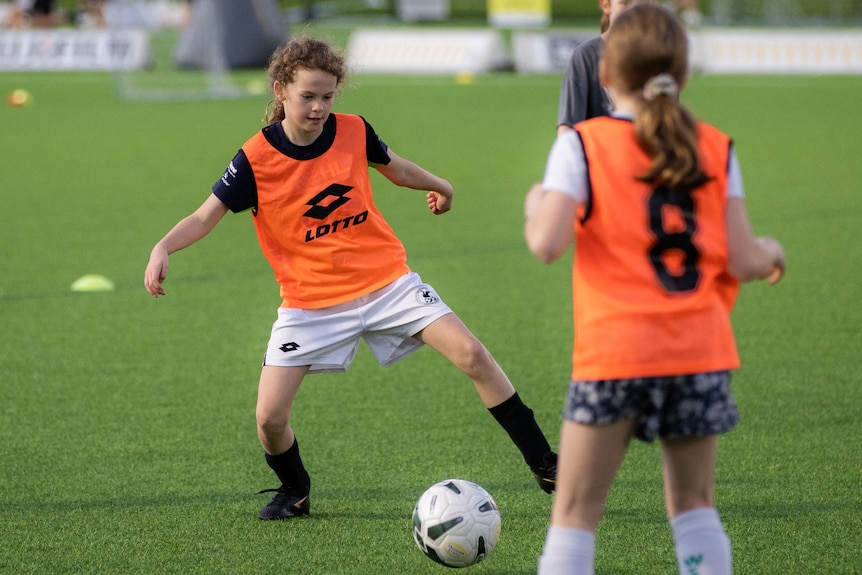 A young female football player looks to kick a ball at the goals at a training session.