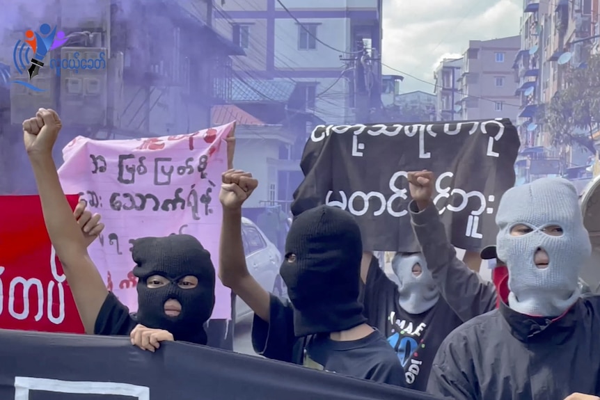 A still image of people in balaclavas protesting with signs in Burmese