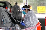 A woman in PPE talks to a driver through a car window.