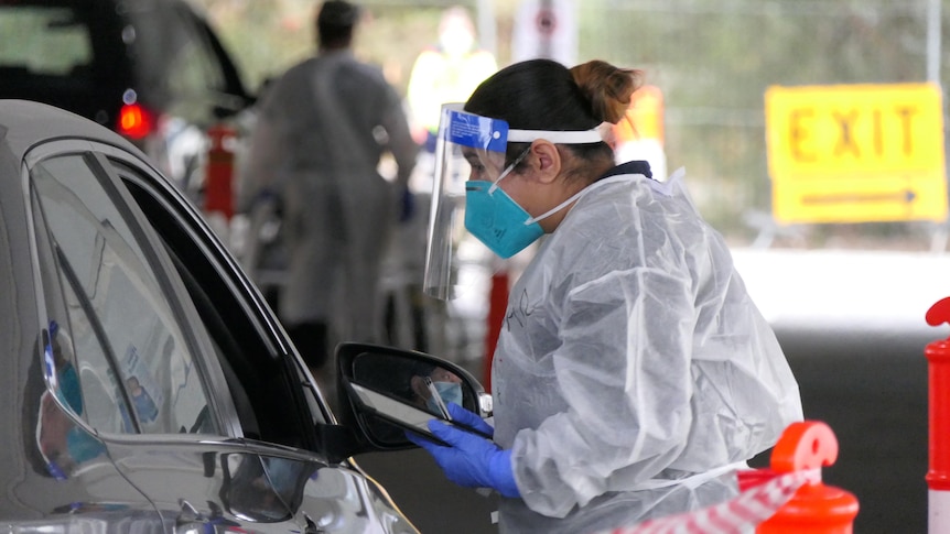 A health professional in full PPE speaks to someone at a COVID testing site.