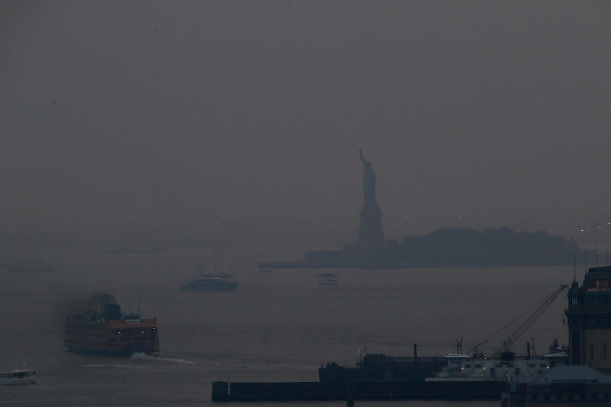 A haze of smoke settles over the Hudson river with the Statue of Liberty barely visible.