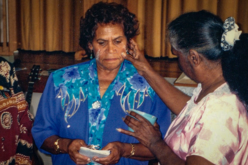 An Indigenous woman is painting another Indigenous woman's face with ceremonial paint