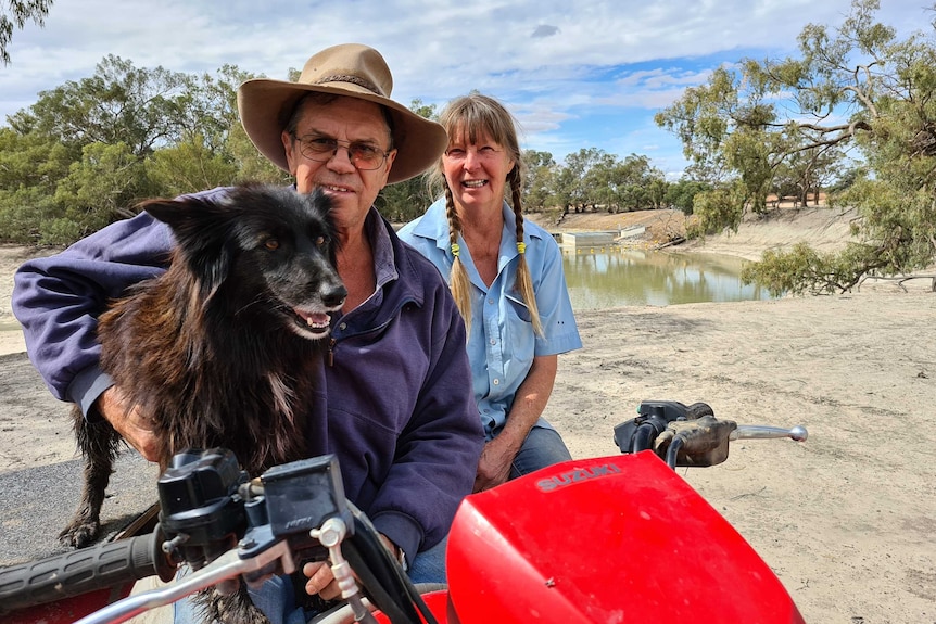 Geoff Lambert, with his arm around an excited dog, and Irene Sher on a quadbike next to Pooncarie's town weir