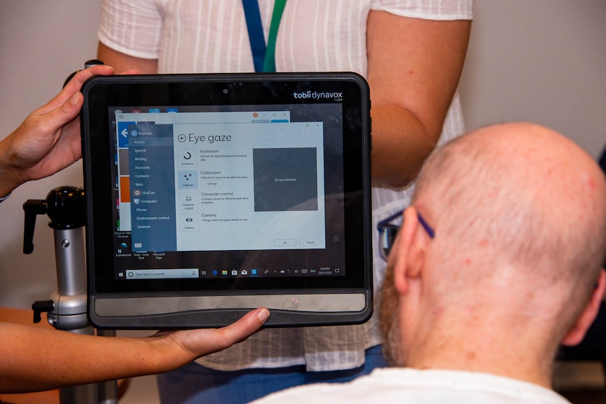 A bald man with glasses looks at a tablet computer screen being held in front of his face