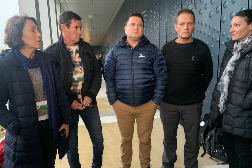 Two women and three men stand in a group in a corridor.