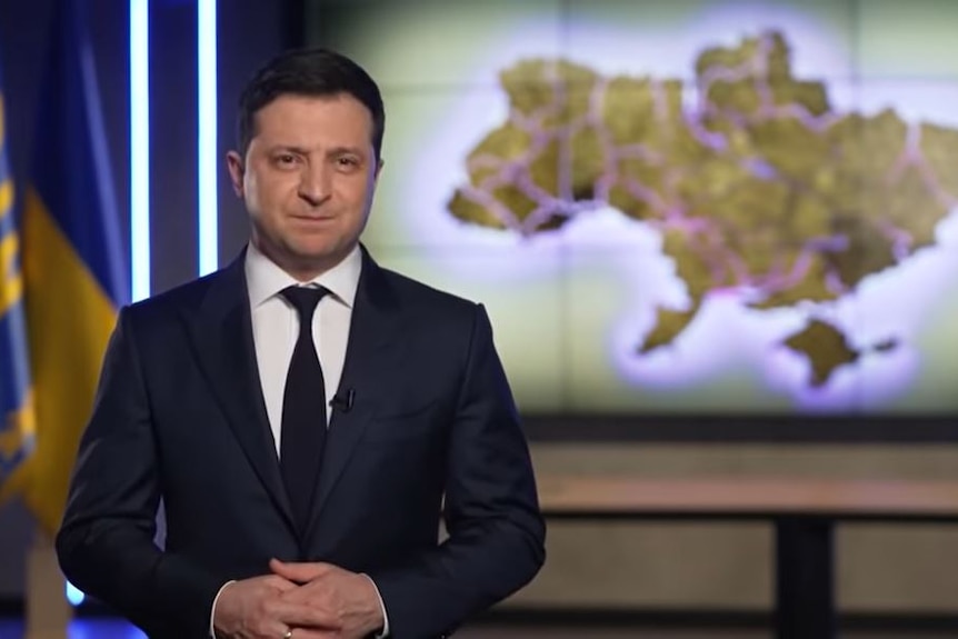 Ukraine President Volodymyr Zelenskyy stands in front of a map of Ukraine.