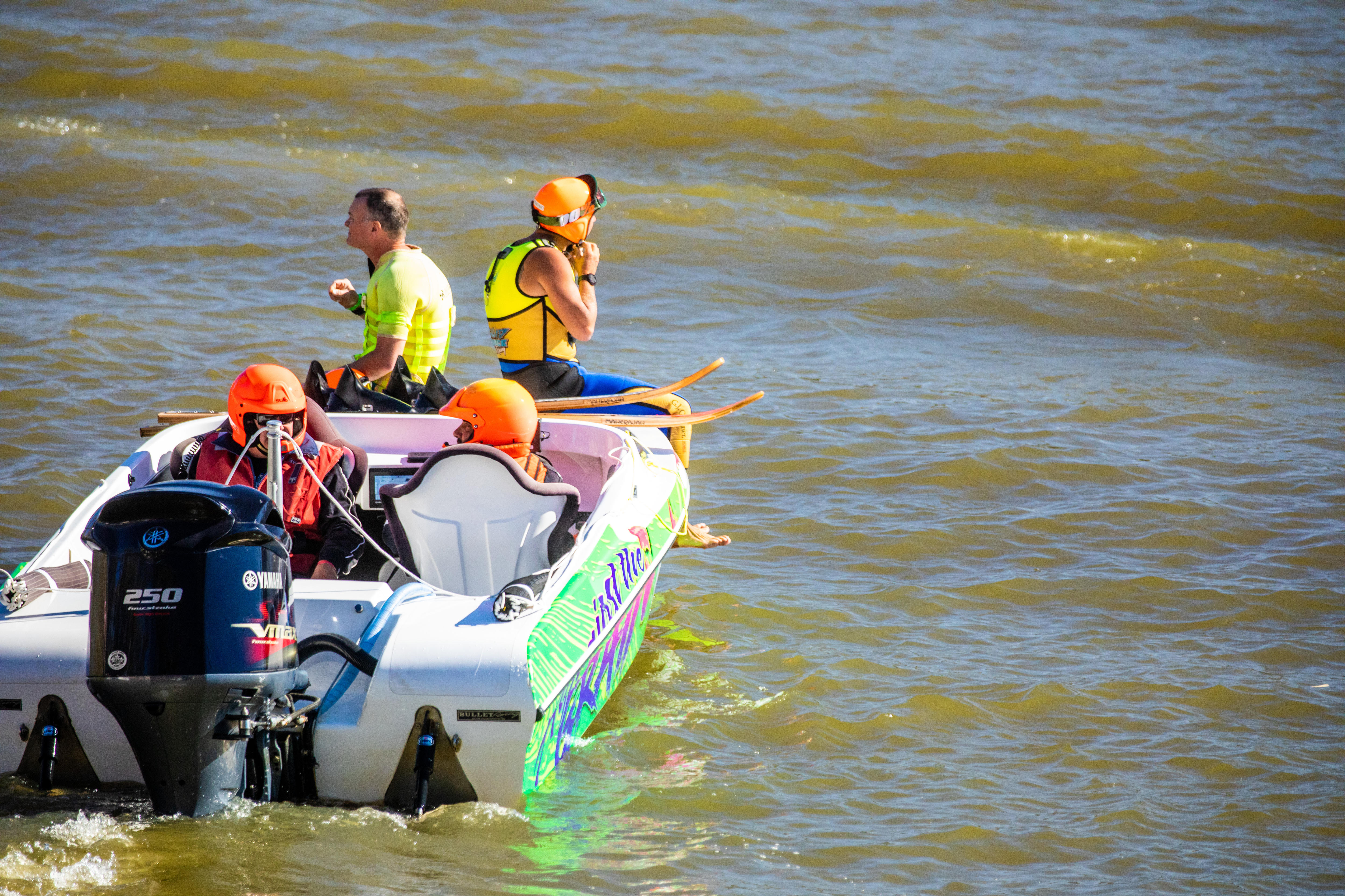 Un esquiador acuático con un casco naranja se prepara para saltar desde un barco al río.