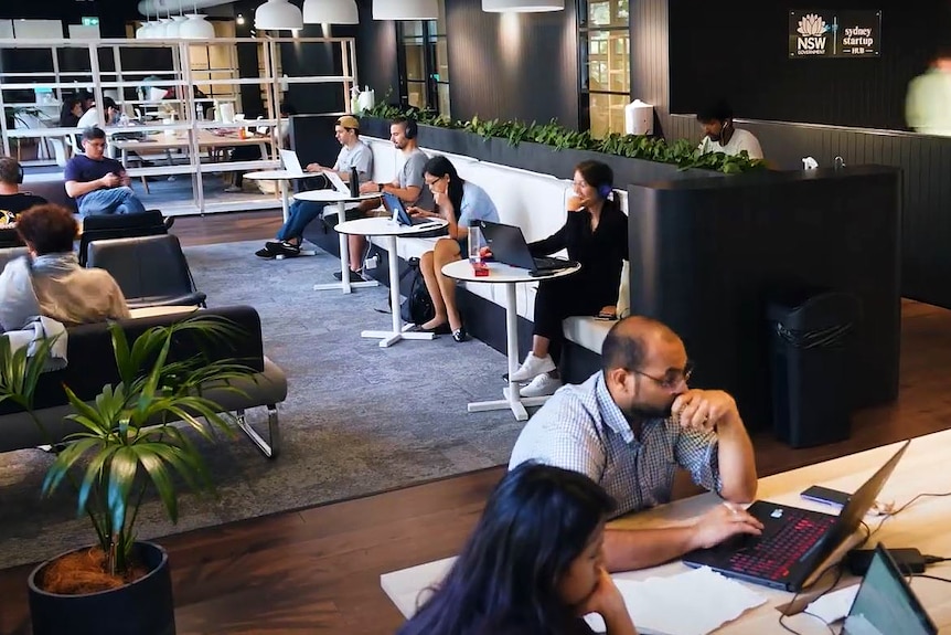 A group of people sitting at desks, others at round tables talking and working.