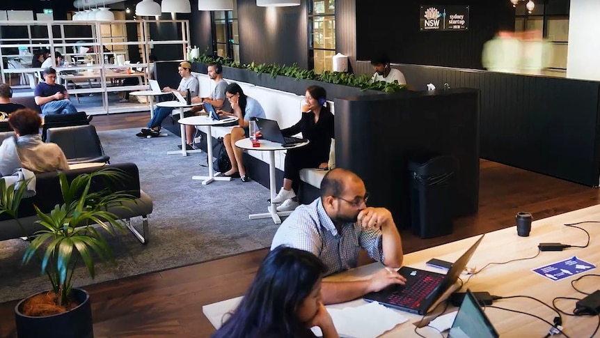 A group of people sitting at desks, others at round tables talking and working.