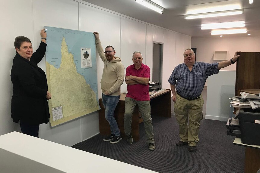 The four members of the Longreach Leader team renovating their newsroom and holding up a map of pastoral stations in Queensland.