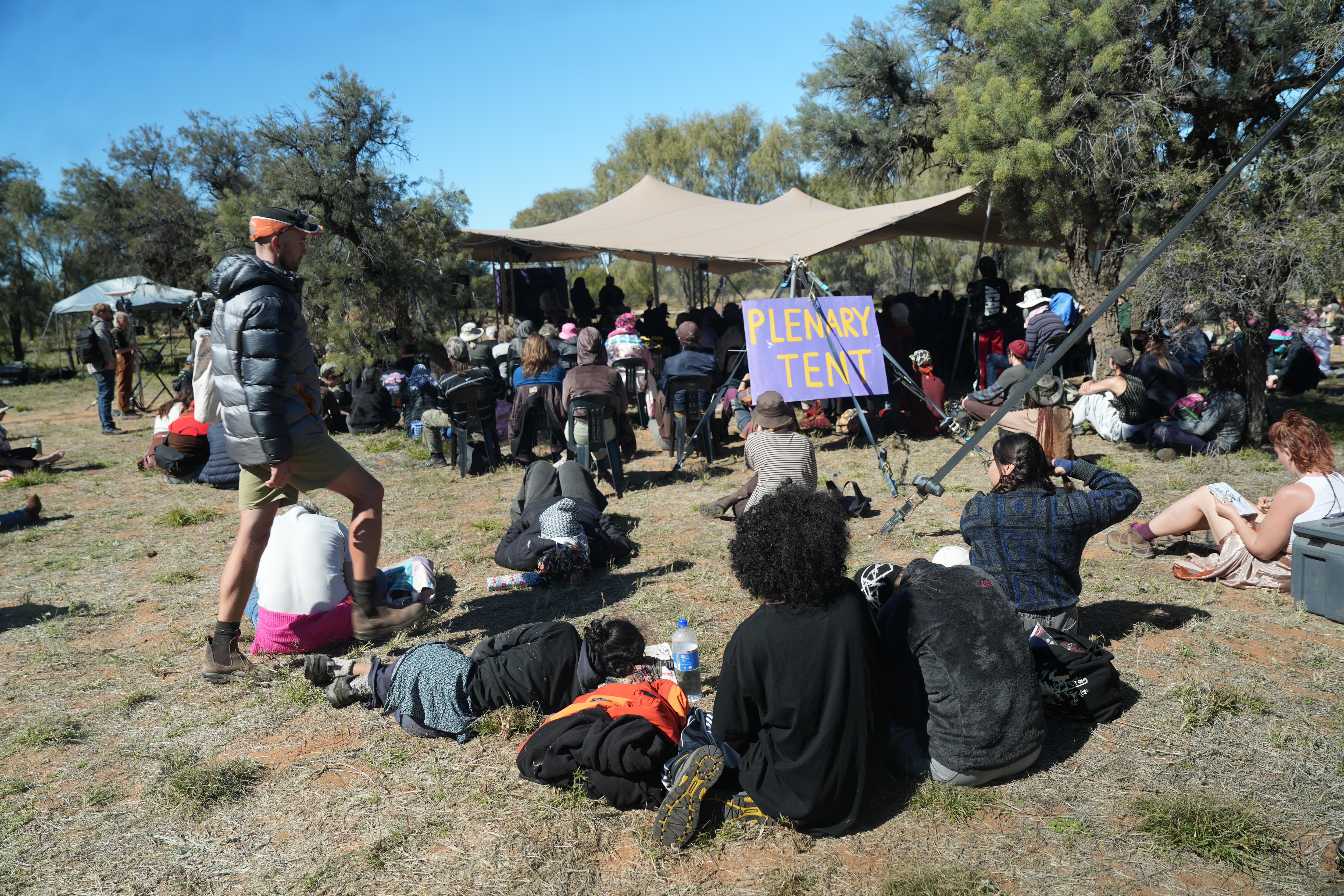 Protesters gather outside under a shade cloth.