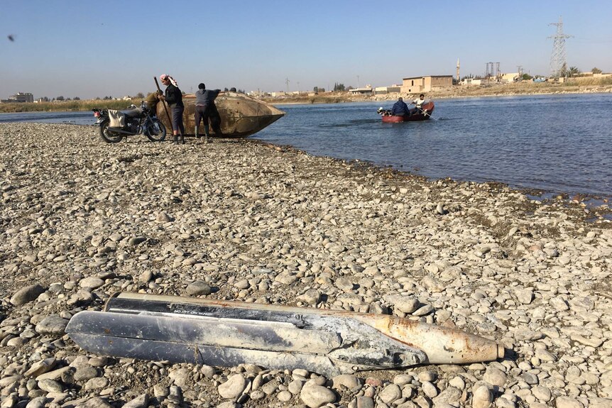 A missile lying on rocky bank of river with people in background in boat and tipping a boat.