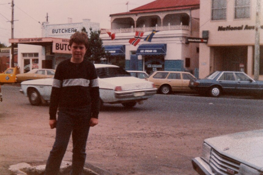 A young boy in a jumper poses in front of a building.