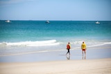 A wide shot of two lifesavers walking along a beach.