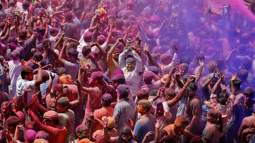 A crowd of people are splashed in colours as they dance during celebrations for Holi in India