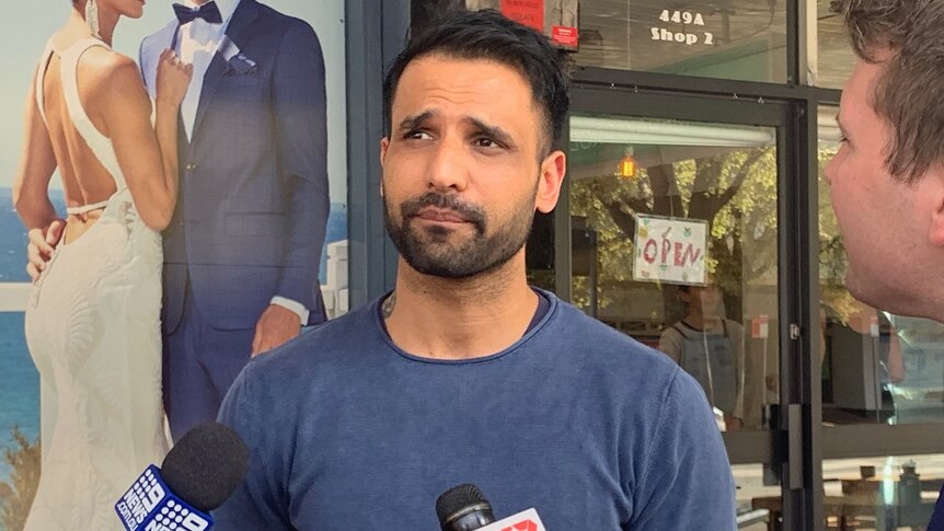 Gurul Gooman speaks to media while standing in front of a shop.