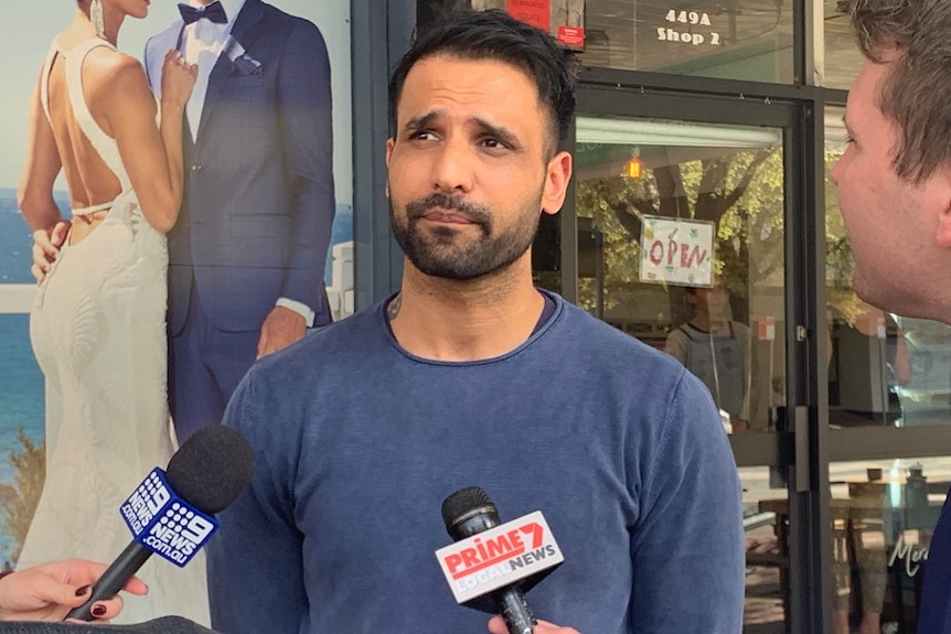 Gurul Gooman speaks to media while standing in front of a shop.