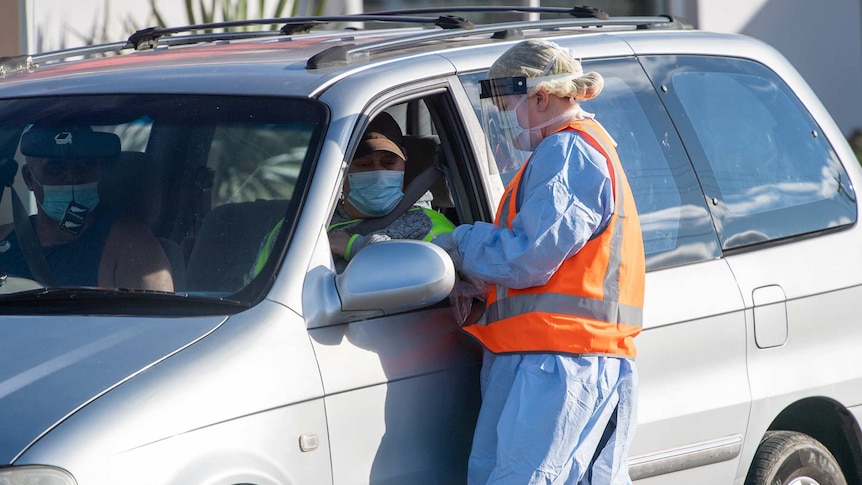 a woman in ppe speaking to a driver in a face mask