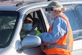 a woman in ppe speaking to a driver in a face mask