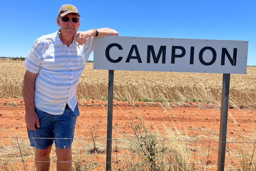 A man wearing shorts and a white shirt, standing next to a roadside that reads 'Campion'.