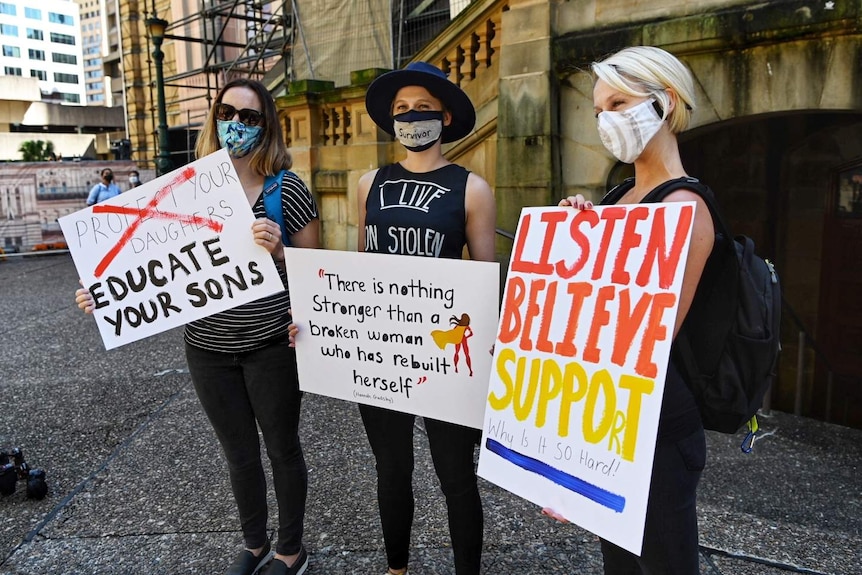 Three women hold signs.