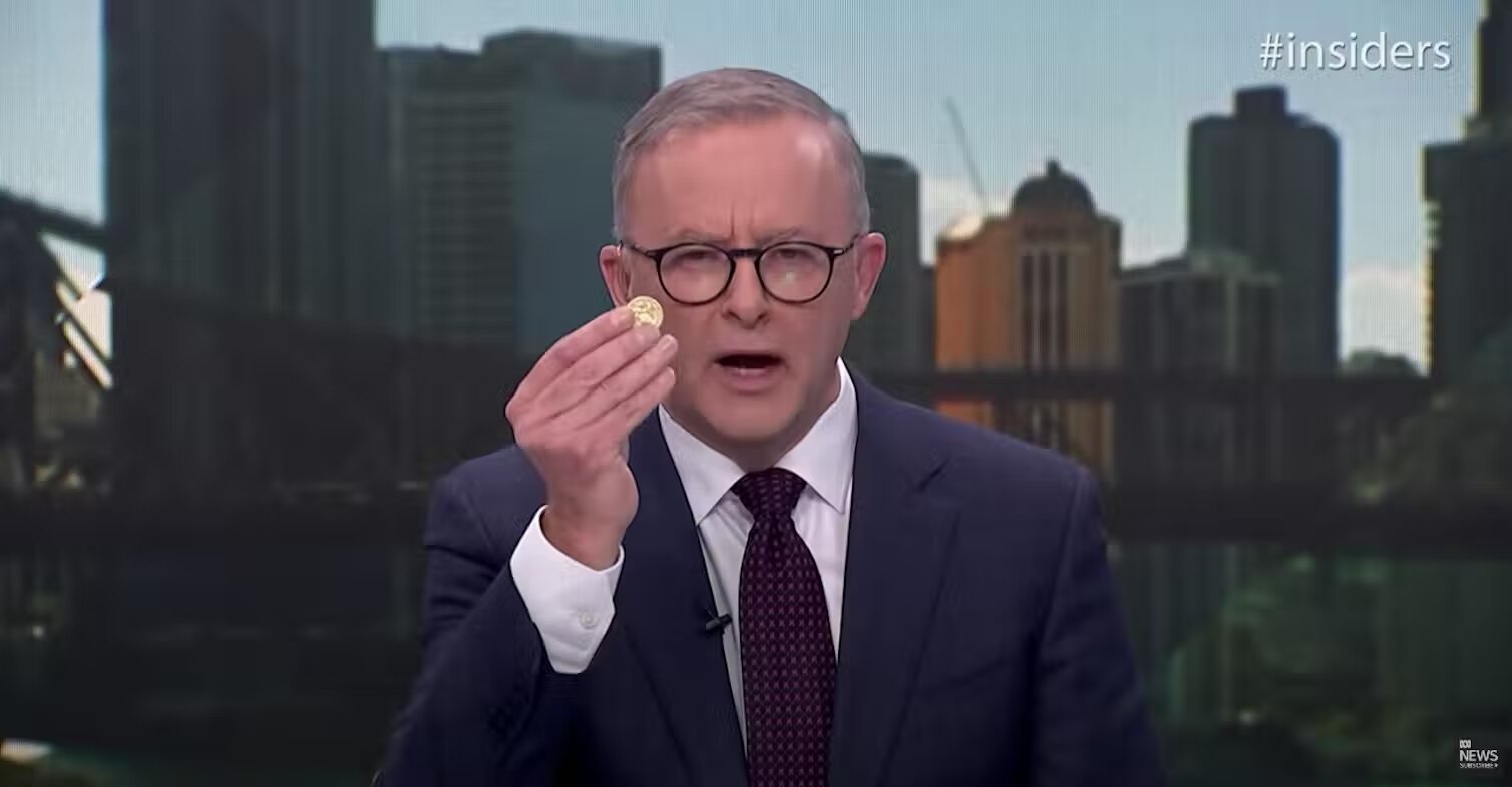 Anthony Albanese, appearing on the Insiders program wearing a navy suit, holds up a one dollar coin
