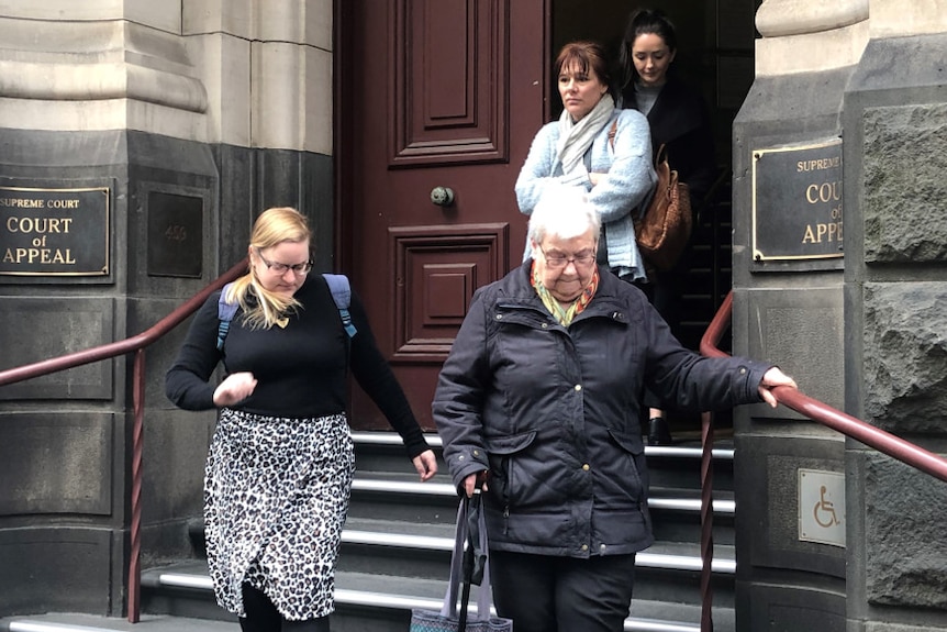 An elderly woman holds the handrail as she walks down the stairs as three younger women exit the Supreme Court behind her.