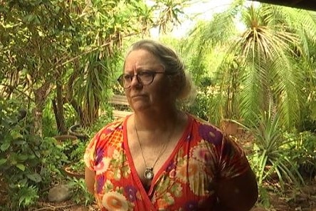 Image of a woman standing in front of a tropical garden wearing a flower-patterned shirt.